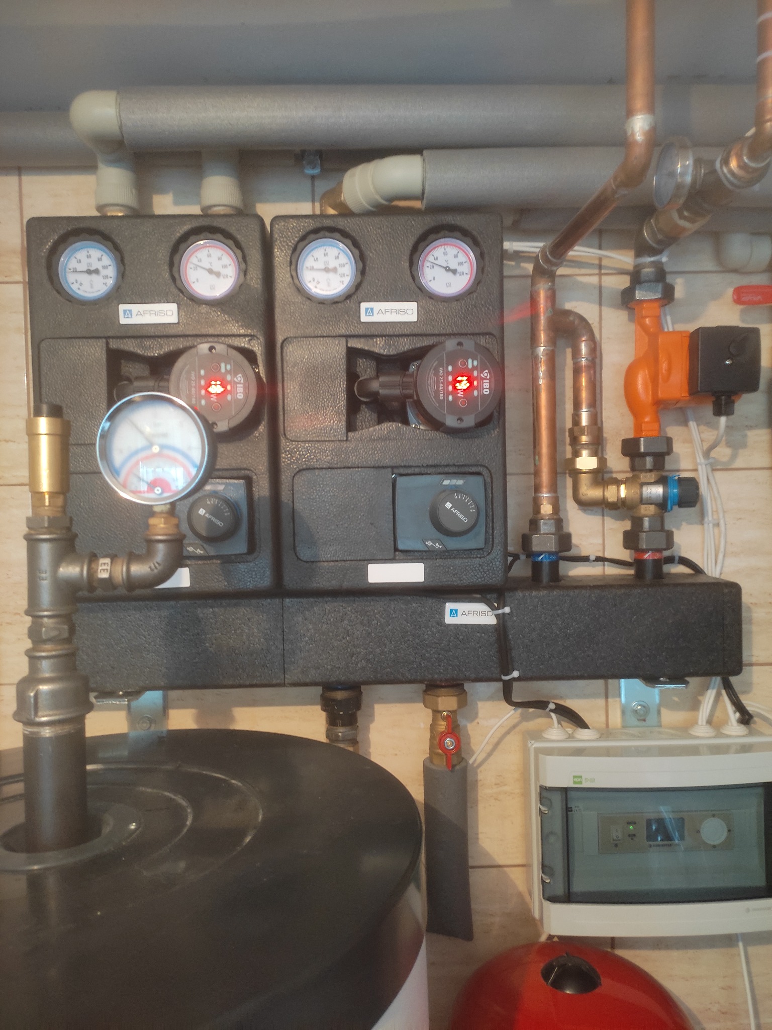 Zestaw rozdzielacza ogrzewania podłogowego Afriso z dwoma obiegami grzewczymi, manometrami, pompami obiegowymi IBO, zaworami i rurami miedzianymi, zamontowany na ścianie wyłożonej płytkami...