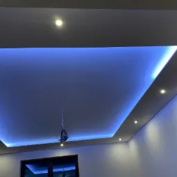 Nowoczesny sufit podwieszany z niebieskim oświetleniem LED, widoczne punktowe źródła światła i fragment instalacji elektrycznej w trakcie prac.