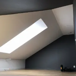 Poddasze z oknem dachowym, pomalowane ściany na szaro i biało, drewnopodobna podłoga, widoczne narzędzia w rogu pomieszczenia.