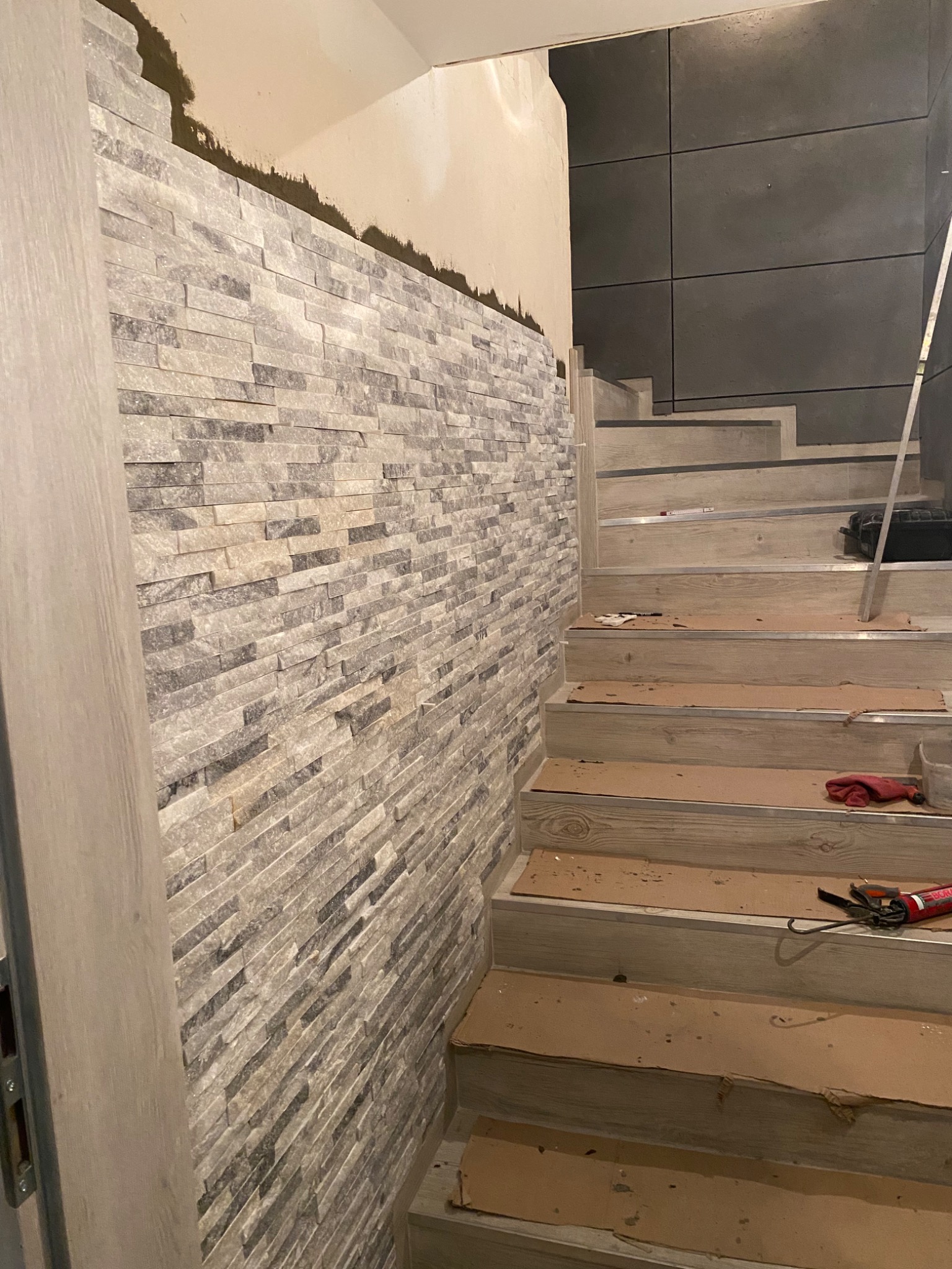 Montaż dekoracyjnej ściany z kamienia na klatce schodowej, widoczne niedokończone górne partie ściany i zabezpieczone schody.