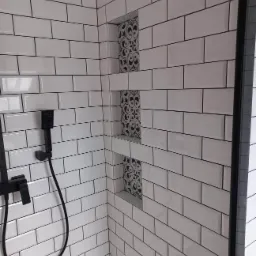 Nowoczesna kabina prysznicowa wyłożona białymi, prostokątnymi płytkami z czarną fugą, z wnękami dekorowanymi płytkami w stylu retro, wyposażona w czarną armaturę.
