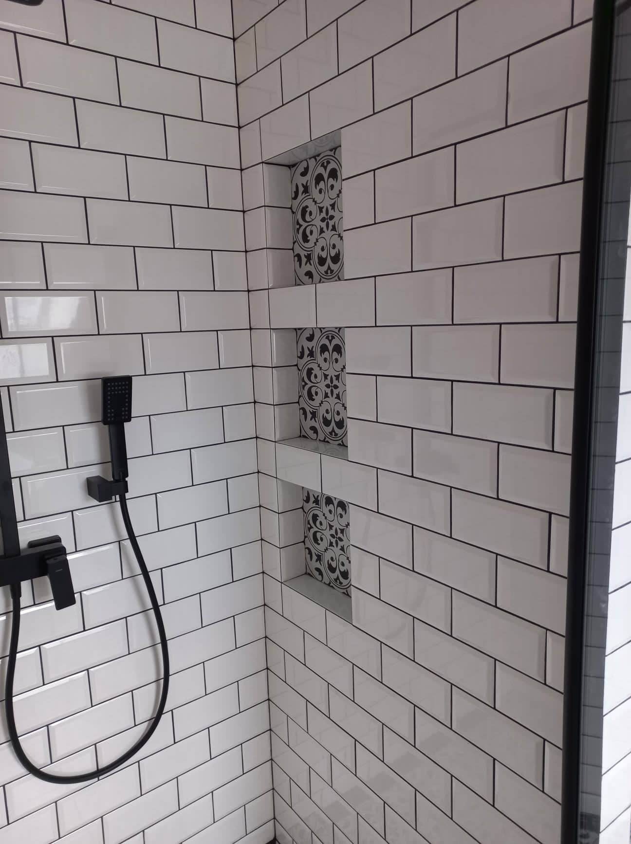 Nowoczesna kabina prysznicowa wyłożona białymi, prostokątnymi płytkami z czarną fugą, z wnękami dekorowanymi płytkami w stylu retro, wyposażona w czarną armaturę.