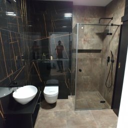 Rem Kompleks - Nowoczesna łazienka z czarnymi płytkami z złotymi żyłami, umywalką nablatową, toaletą i kabiną prysznicową ze szklaną ścianą.