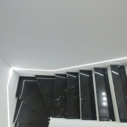 Rem Kompleks - Widok z góry na nowoczesne schody z czarnego marmuru z białymi żyłkami, podświetlone listwą LED wzdłuż ściany, minimalistyczny design.