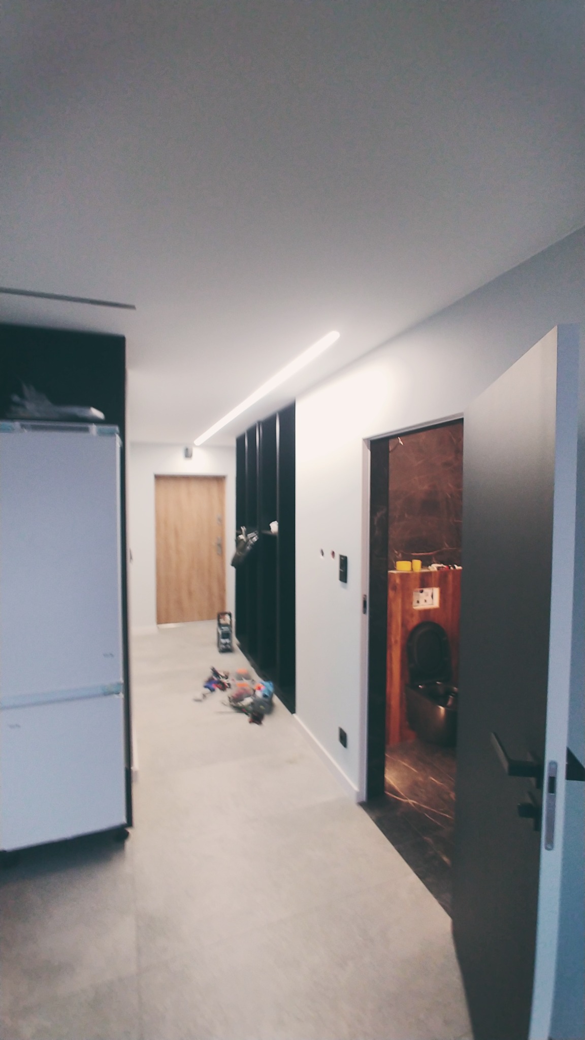 Wnętrze mieszkania w trakcie prac wykończeniowych, widoczna łazienka z elementami drewna i marmuru, na podłodze rozsypane narzędzia i akcesoria.