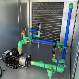 Instalacja pompy obiegowej z rurami w kolorach zielonym i niebieskim, widoczna manometry, całość umieszczona w metalowej obudowie, Zamość.