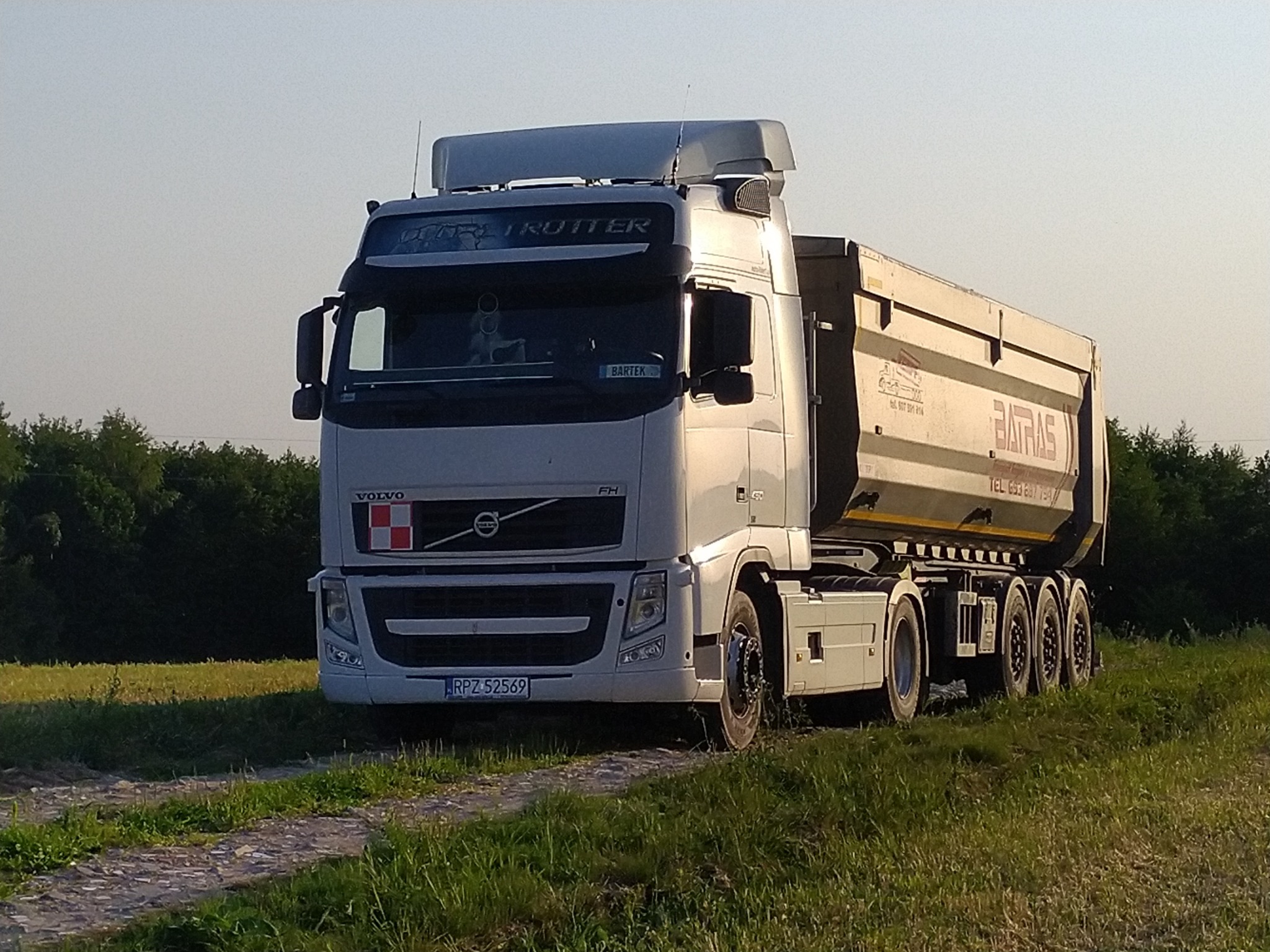 Ciężarówka Volvo FH z naczepą wywrotką Batras, zaparkowana na polnej drodze, widoczne tablice rejestracyjne RPZ 52569, napis 'ULTRA TROTTER' nad szybą, i imię 'BARTEK' na tabliczce w kabinie.