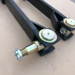 Dwa czarne, spawane elementy metalowe z osiami i nakrętkami na brązowym tle.