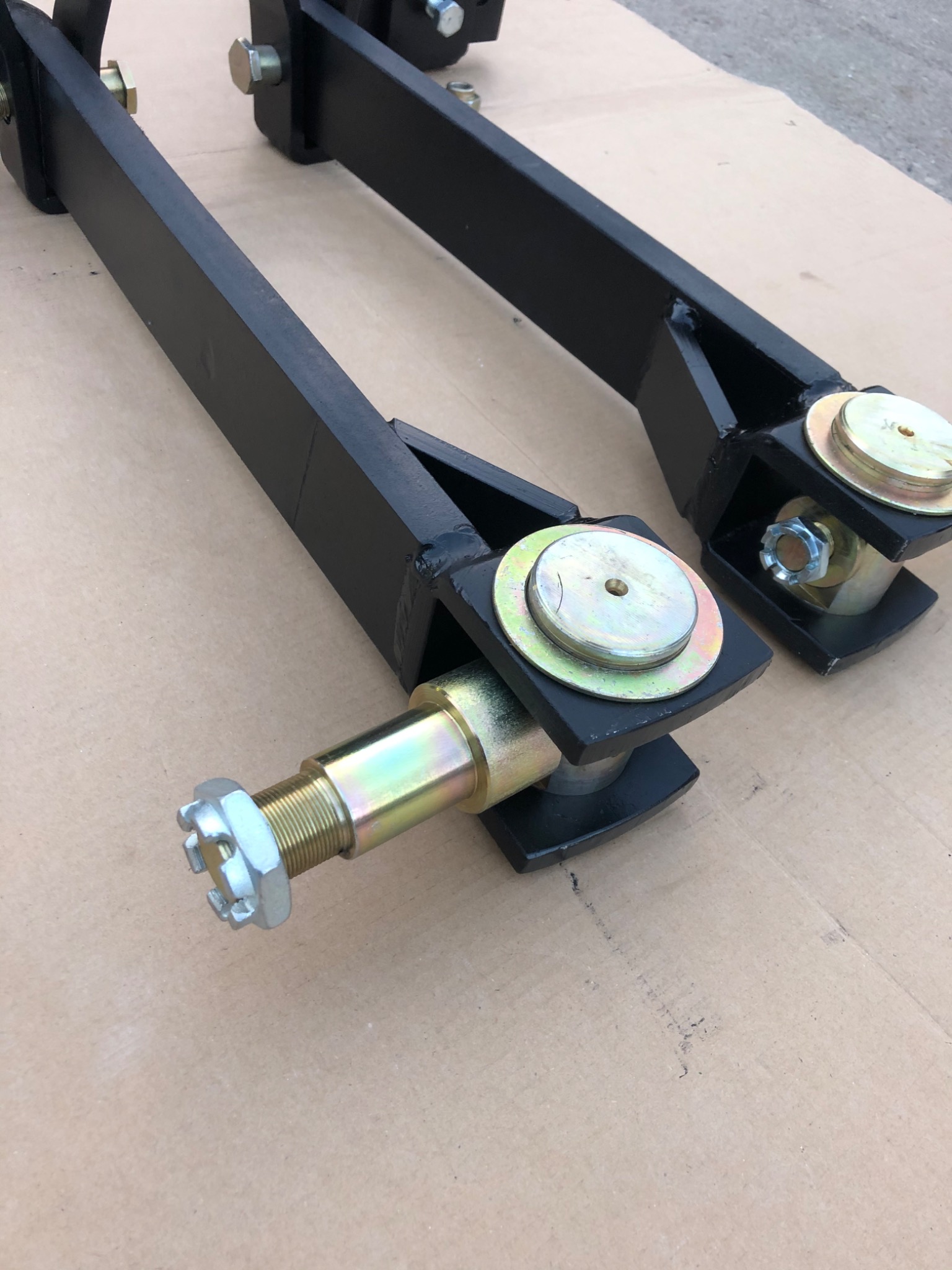 Dwa czarne, spawane elementy metalowe z osiami i nakrętkami na brązowym tle.