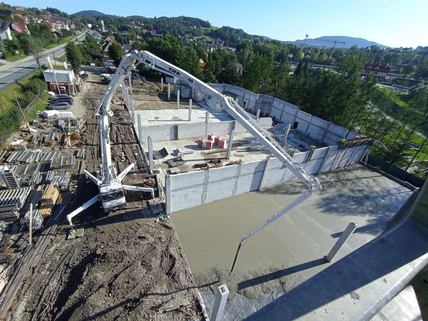 Proces wylewania betonu na budowie z użyciem pompy CIFA K40 XRZ. Widok z góry na plac budowy, betonowe ściany i kolumny w tle.