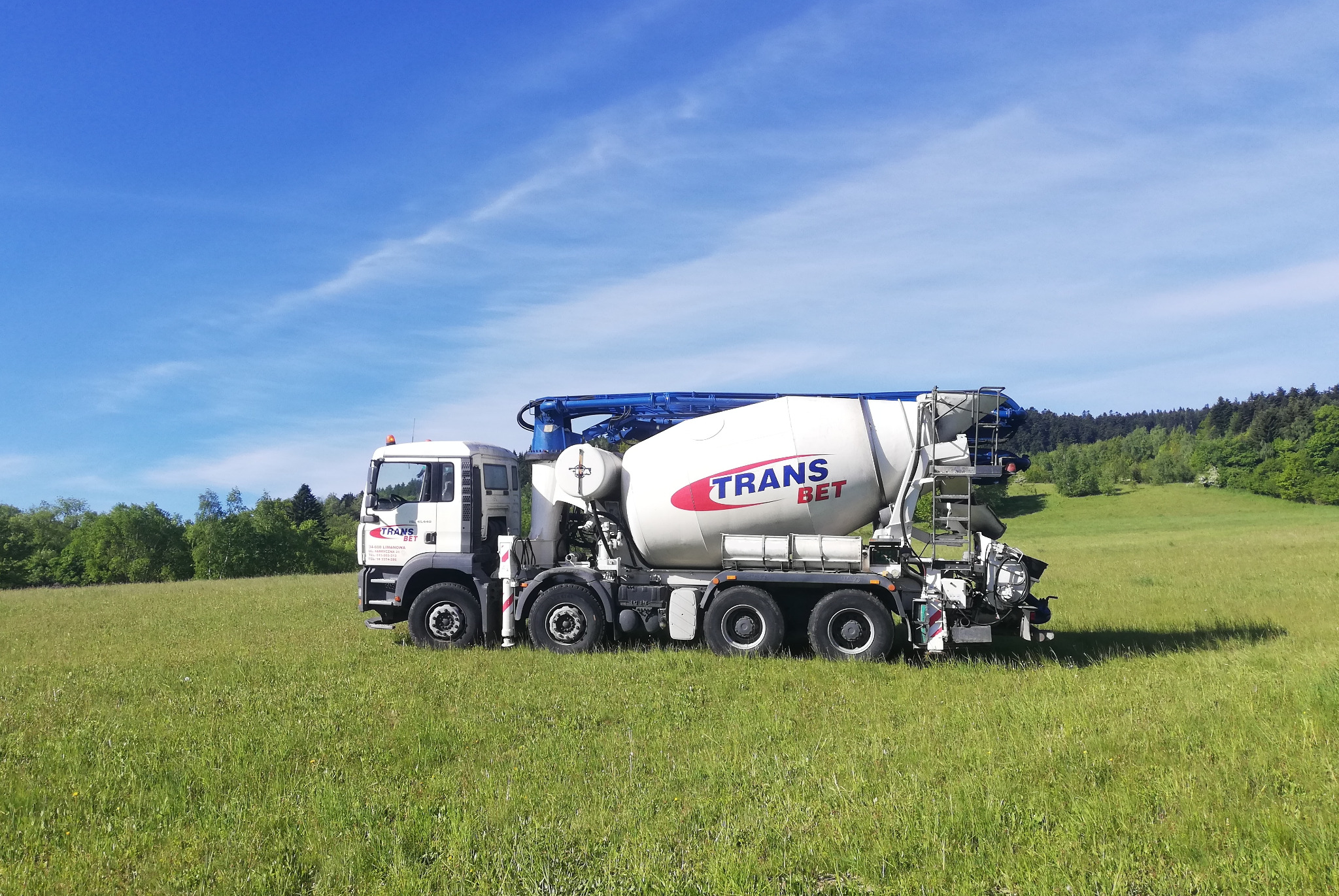 Cysterna do przewozu betonu Trans Bet na tle łąki i lasu, błękitne niebo z delikatnymi chmurami.