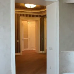 Wykończone wnętrze: widok przez białe, ozdobne futryny na parkiet, pomalowane ściany z efektem dekoracyjnym i drzwi wewnętrzne w tle.