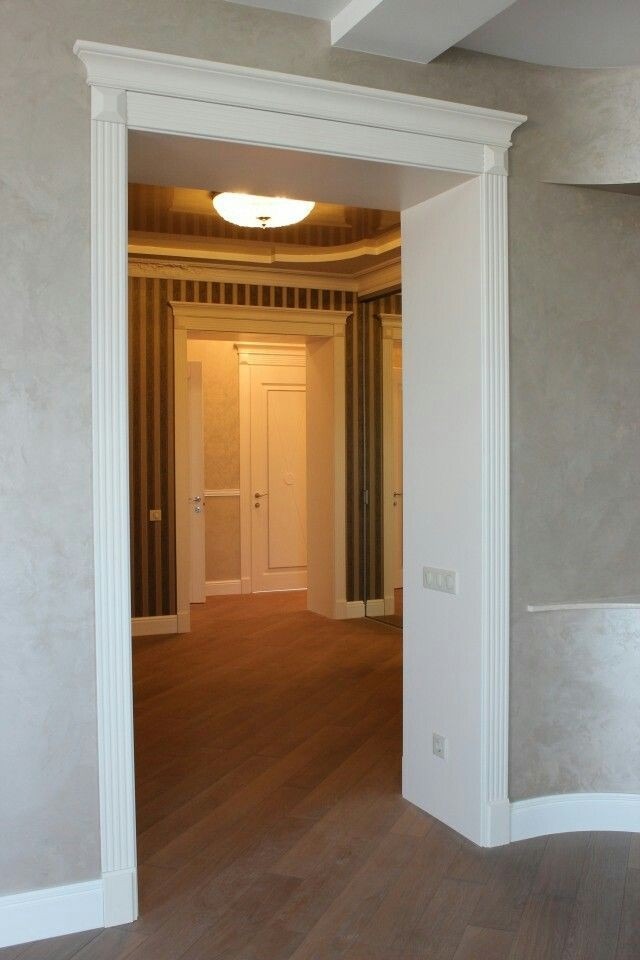 Wykończone wnętrze: widok przez białe, ozdobne futryny na parkiet, pomalowane ściany z efektem dekoracyjnym i drzwi wewnętrzne w tle.