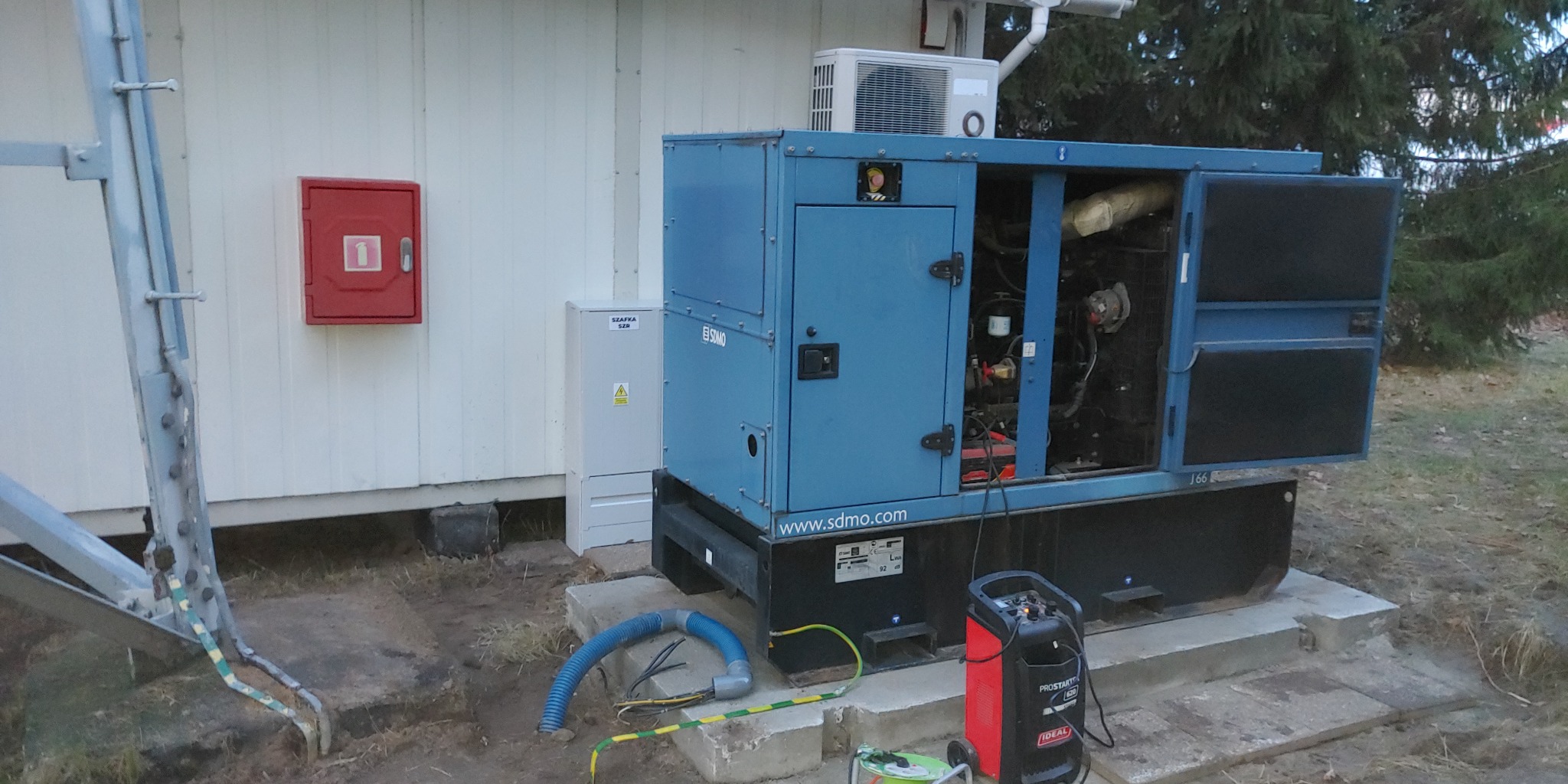 Zewnętrzny montaż systemu SZR z agregatem prądotwórczym SDMO, widoczna szafka SZR, zabezpieczenia i podłączenia elektryczne.