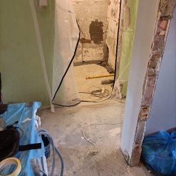 Łukasz Zduńczyk - Łazienka w trakcie demontażu: zerwane płytki, zabezpieczone folią drzwi i ściany, widoczne narzędzia i gruz.