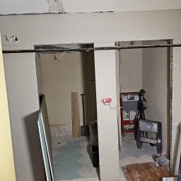 Łukasz Zduńczyk - Łazienka w trakcie remontu: widoczne płyty gipsowo-kartonowe na ścianach, instalacja elektryczna, fragment starej podłogi z płytek i przygotowane podłoże pod nową posadzkę, drabina malarska...