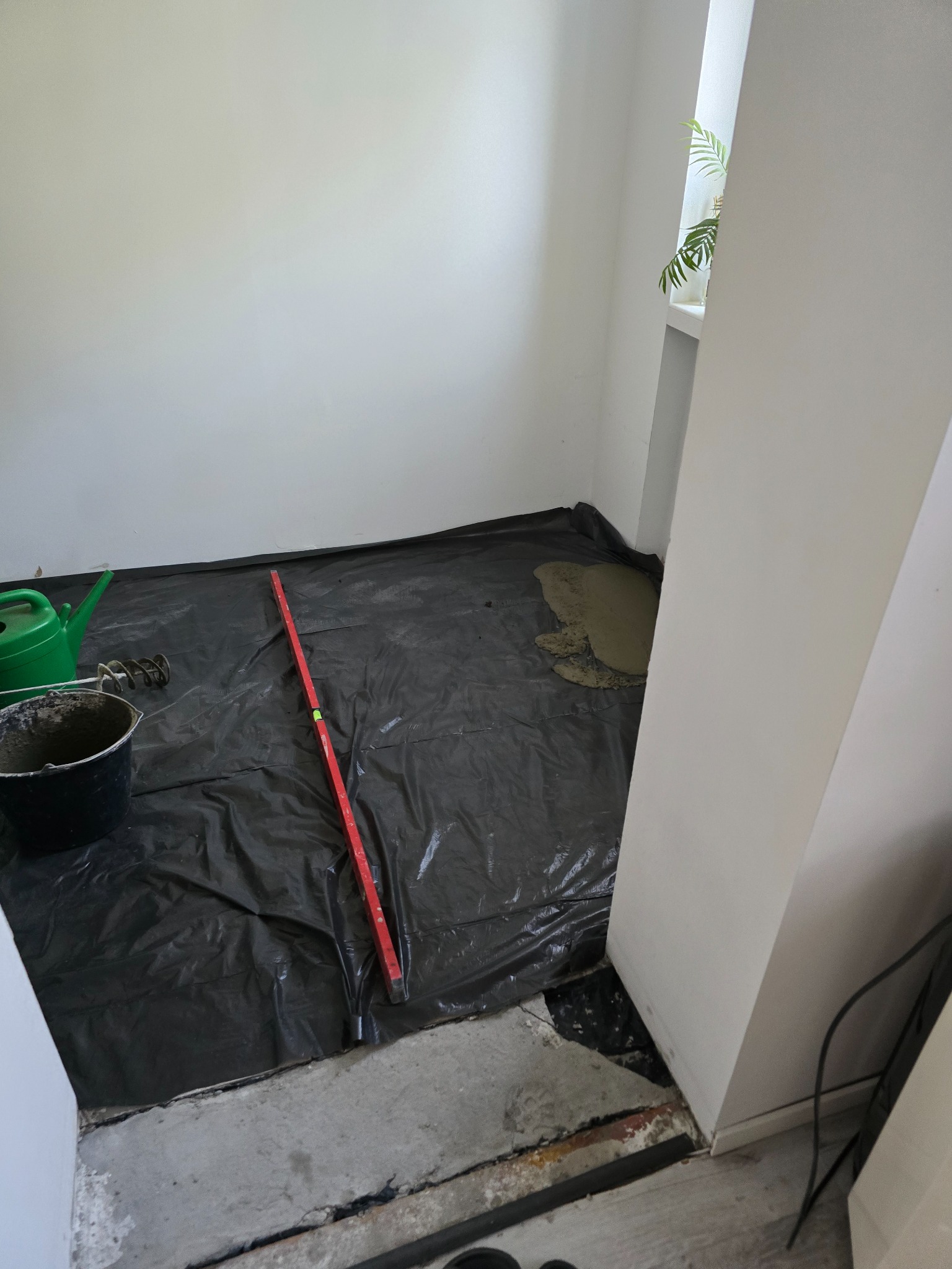 Przygotowanie podłoża w łazience: folia ochronna, poziomica, wiadro z zaprawą i mieszadło obok wylewki samopoziomującej