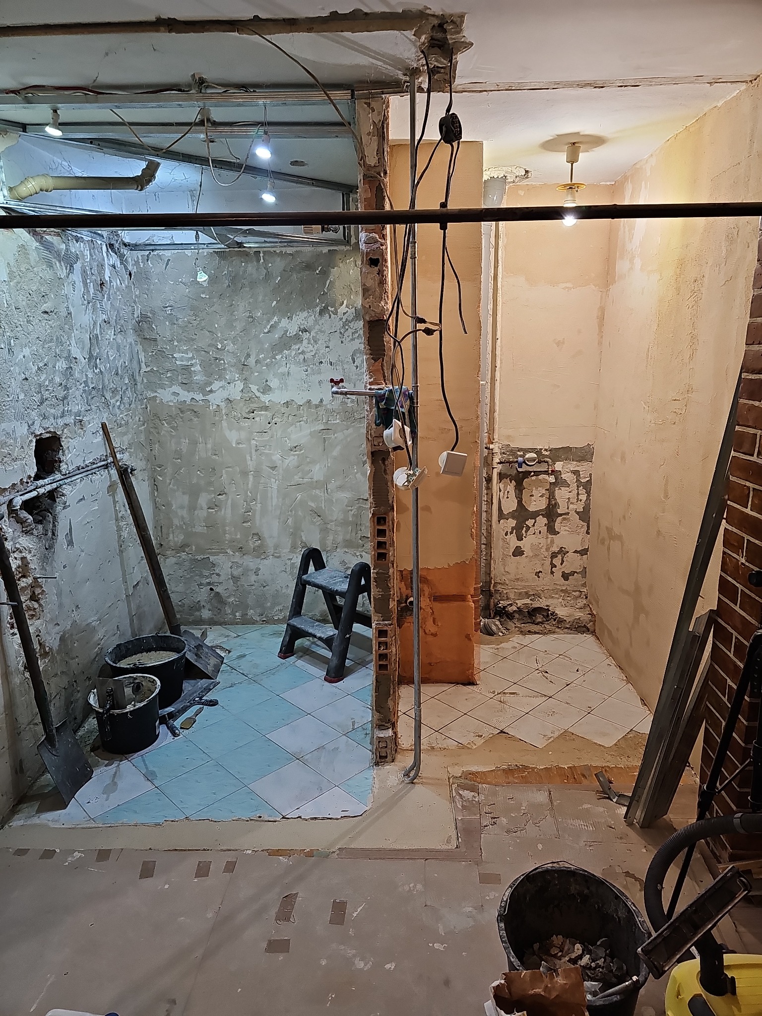 Dzielona przestrzeń łazienki w trakcie remontu: po lewej surowe ściany i resztki płytek, po prawej przygotowane podłoże i instalacje elektryczne, widoczne narzędzia i materiały budowlane.