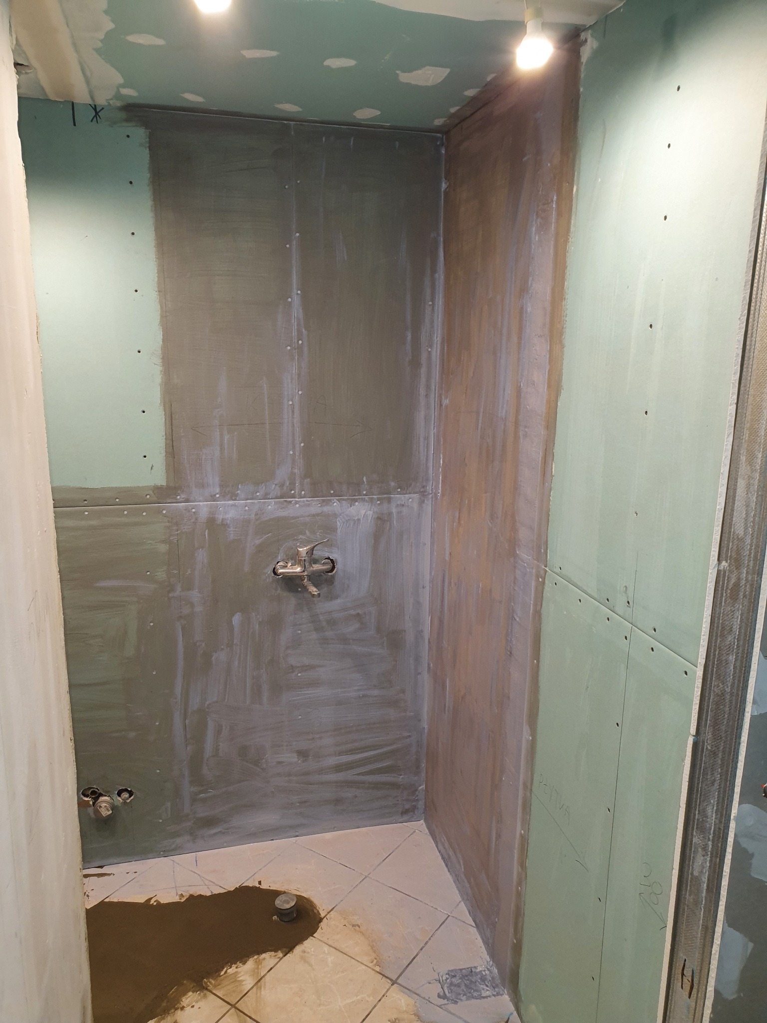 Wnętrze łazienki w trakcie remontu, widoczne płyty gipsowo-kartonowe na ścianach, przygotowane do dalszych prac wykończeniowych, z widocznymi punktami instalacji wodnej i pozostałościami po...