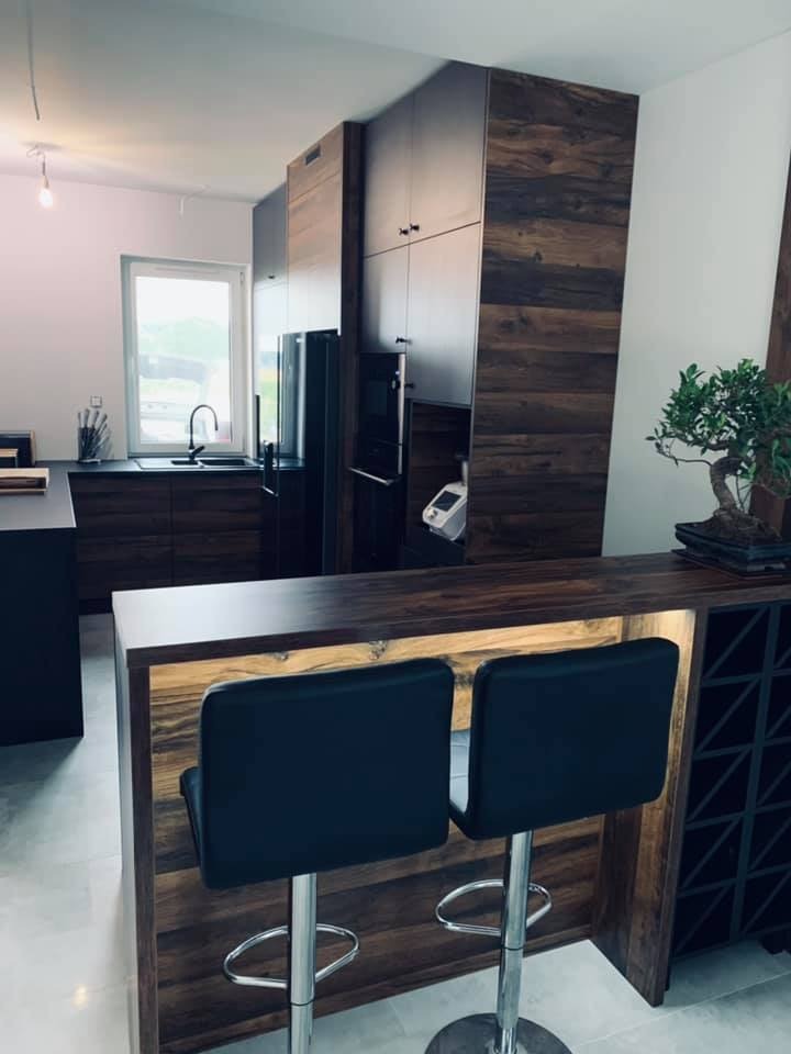 Nowoczesna kuchnia z drewnianymi frontami szafek, wyspą z podświetleniem LED i dwoma hokerami oraz drzewkiem bonsai na blacie.