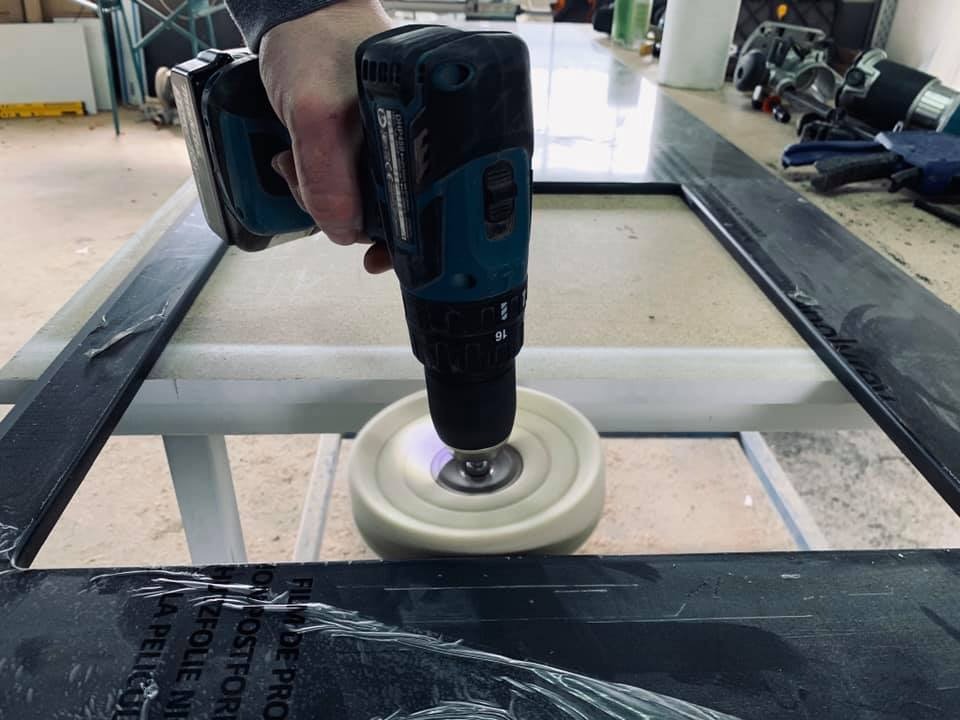 Polerowanie ramy drewnianej drzwi za pomocą wiertarki z nakładką polerską, widoczne elementy ramy w folii ochronnej i narzędzia w tle.