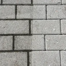 Częściowo wyczyszczona kostka brukowa, widoczna różnica w kolorze między czystą a brudną powierzchnią, mech w szczelinach.