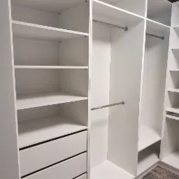 Wnętrze garderoby z białymi półkami, szufladami i drążkami na ubrania, widok na dywan z wzorem.