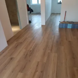 Ułożone panele podłogowe o wzorze drewna w mieszkaniu we Wrocławiu, widoczne paczki paneli Classen Megaloc i mop. W tle widok na łazienkę i pokój.