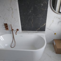 Tomasz Słowik - Nowoczesna łazienka z białą wanną, marmurowymi płytkami w odcieniach bieli i czerni, armaturą w kolorze miedzi oraz kartonem z rękawicami na podłodze.