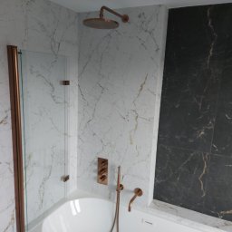 Tomasz Słowik - Nowoczesna łazienka z marmurowymi płytkami w odcieniach bieli i czerni, armatura w kolorze miedzi, deszczownica i szklany panel prysznicowy.