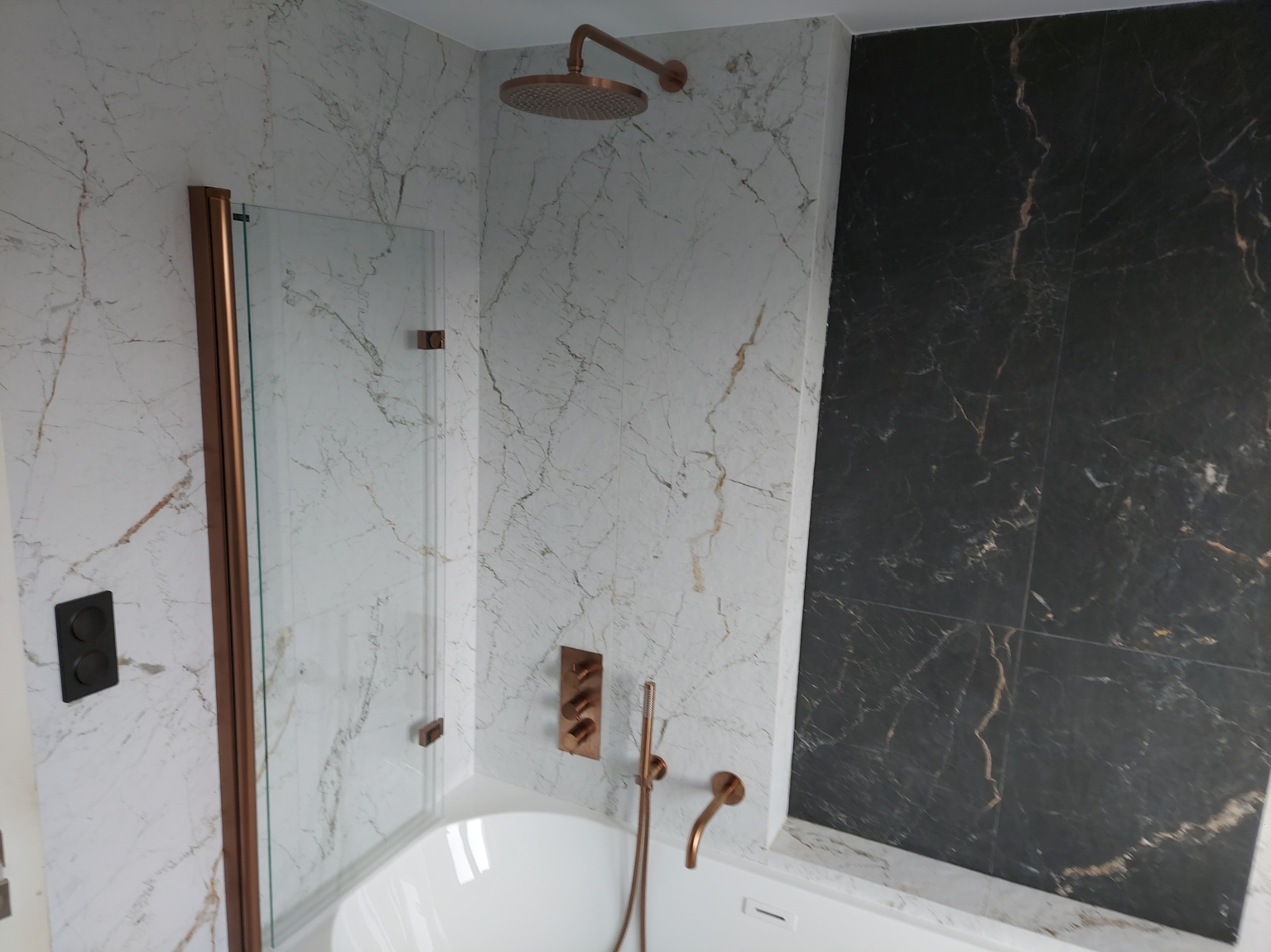 Nowoczesna łazienka z marmurowymi płytkami w odcieniach bieli i czerni, armatura w kolorze miedzi, deszczownica i szklany panel prysznicowy.