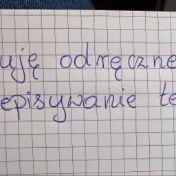 Kartka w kratkę z odręcznym napisem 'Oferuję odręczne przepisywanie tekstów' wykonanym niebieskim długopisem.