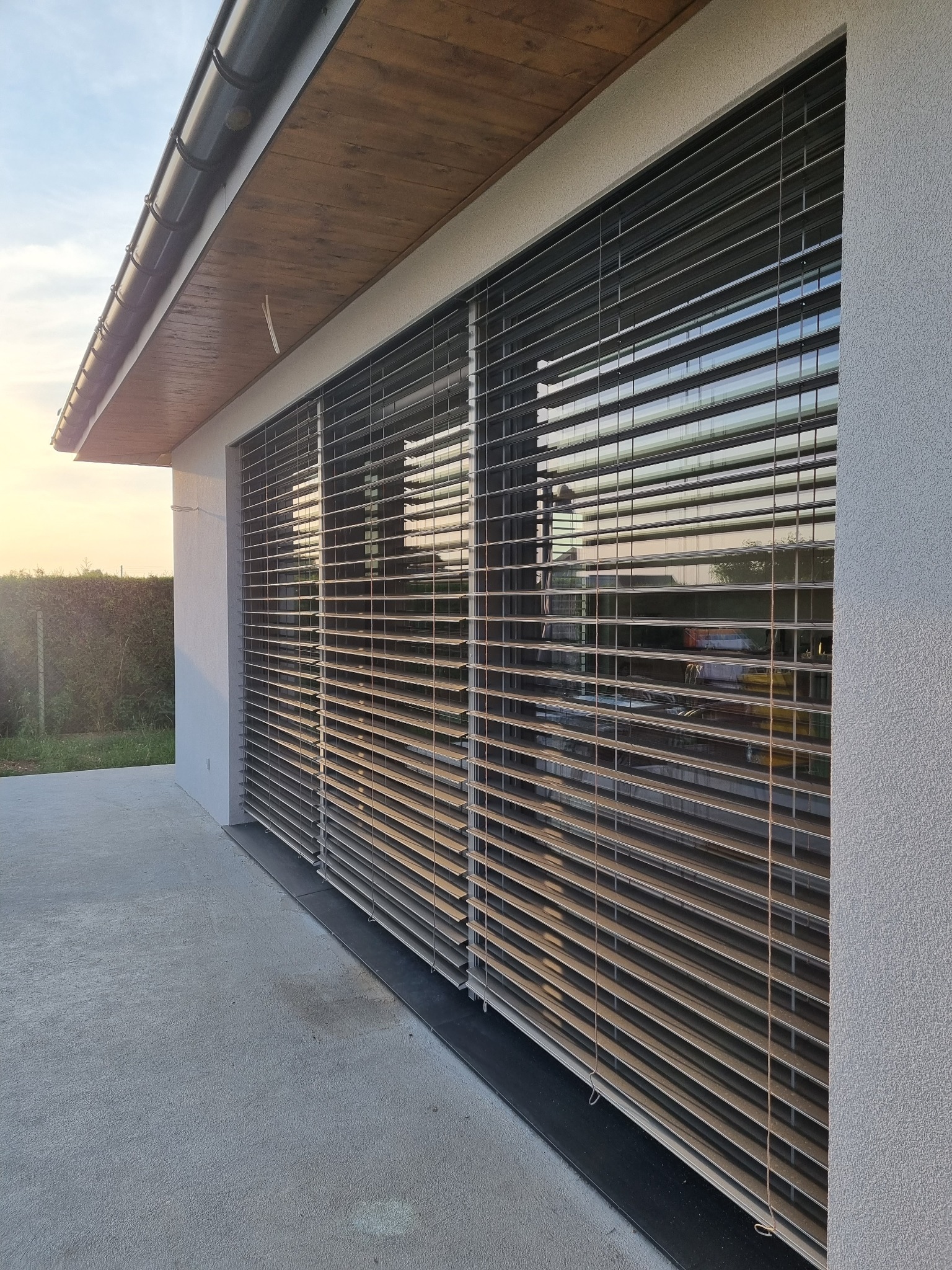 Zewnętrzne żaluzje fasadowe zamontowane na elewacji domu, widoczne z zewnątrz, z refleksami zachodzącego słońca.