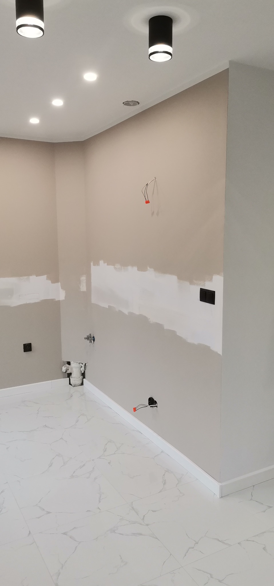 Wnętrze w trakcie szpachlowania ścian, widoczne niedokończone gładzie, wystające kable elektryczne, białe listwy przypodłogowe i marmurowe płytki na podłodze