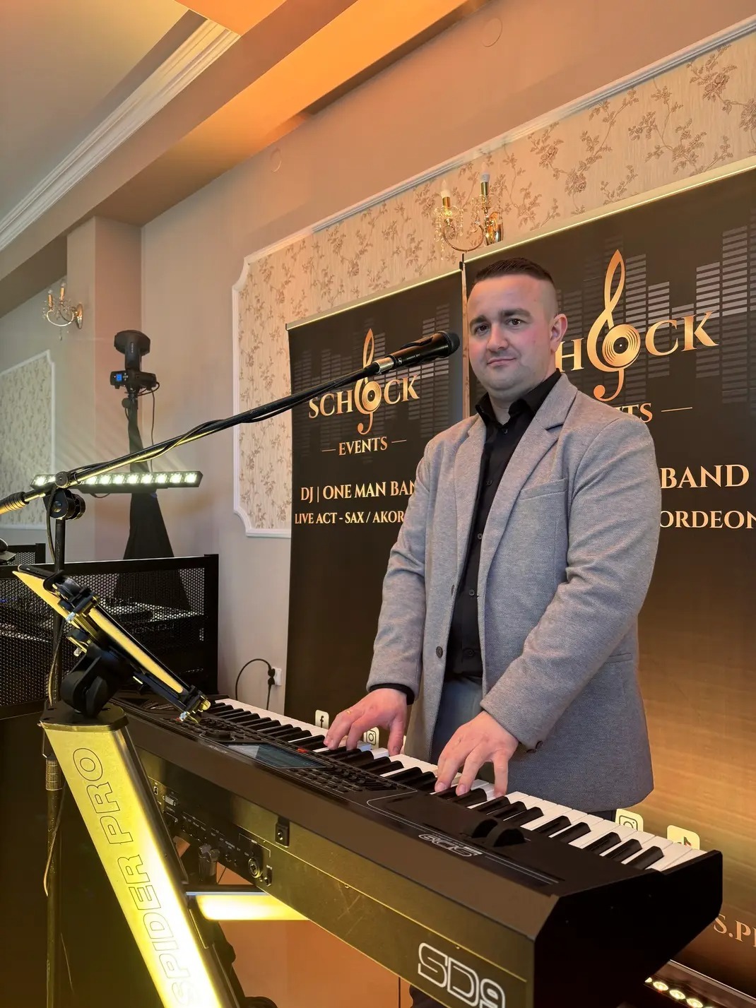 Mężczyzna gra na keyboardzie SD9, na tle baner Schock Events, z oświetleniem scenicznym. DJ, one man band, live act - saksofon i akordeon. Spider Pro.