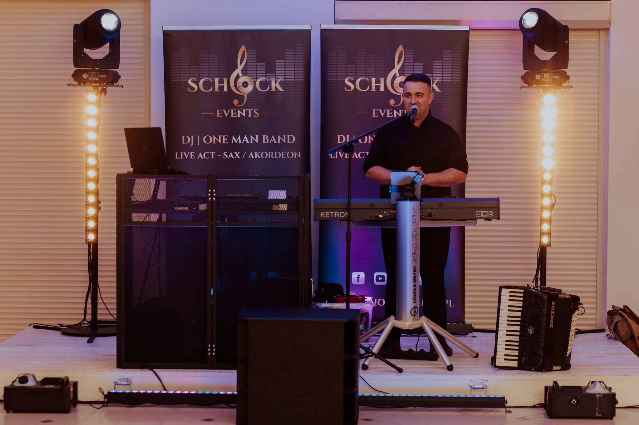 Wokalista na scenie z keyboardem Ketron SD9, akordeonem Hohner, nagłośnieniem i oświetleniem. W tle banery Schock Events.