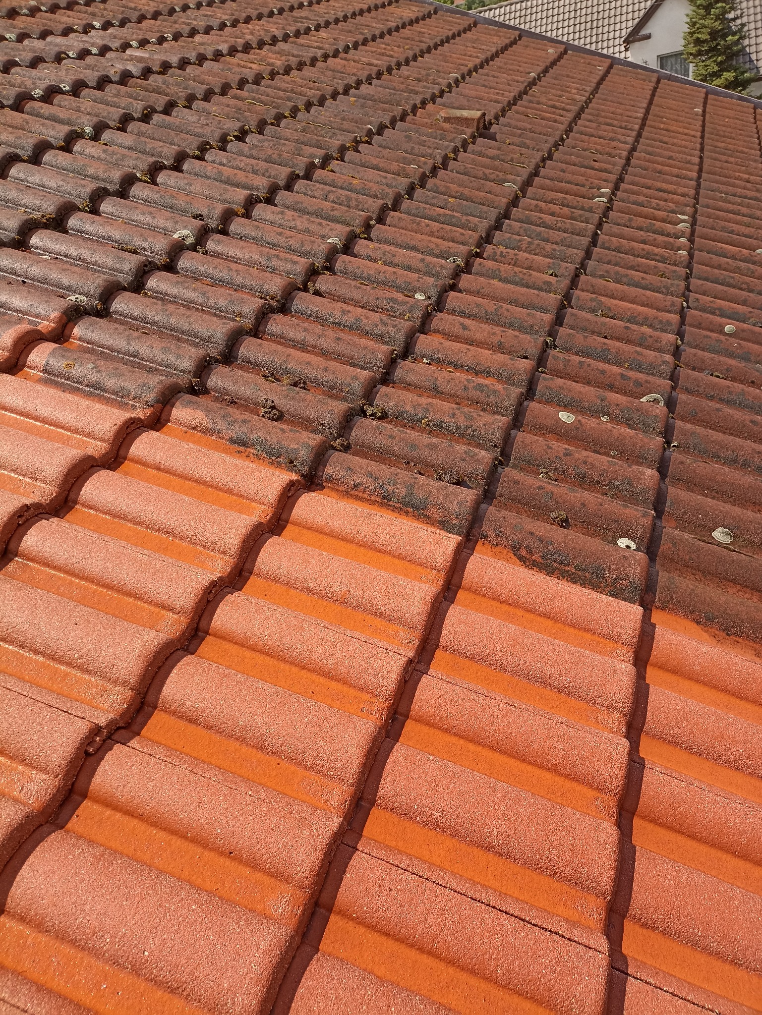 Częściowo wyczyszczony dach z czerwonej dachówki ceramicznej, widoczna różnica między brudną a umytą powierzchnią.
