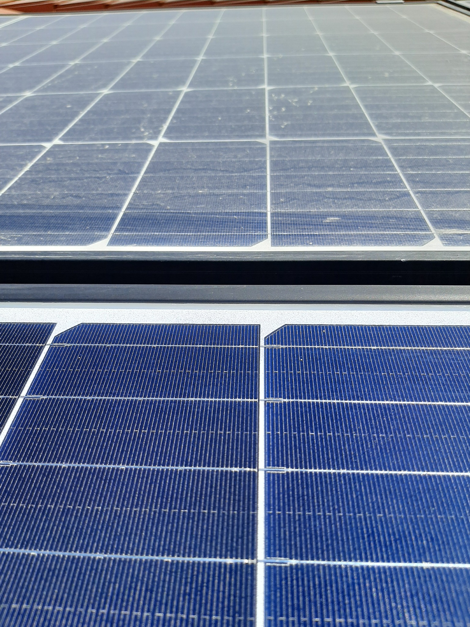 Częściowo zakurzone panele słoneczne na dachu, widoczne z bliska, z górnym panelem pokrytym warstwą brudu, a dolnym czystym i niebieskim.