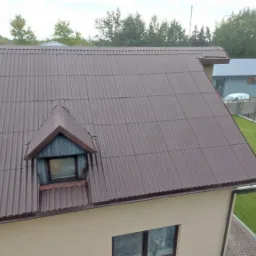 Brązowy dach z blachy falistej z lukarną, widok z góry na budynek i zadbany trawnik.