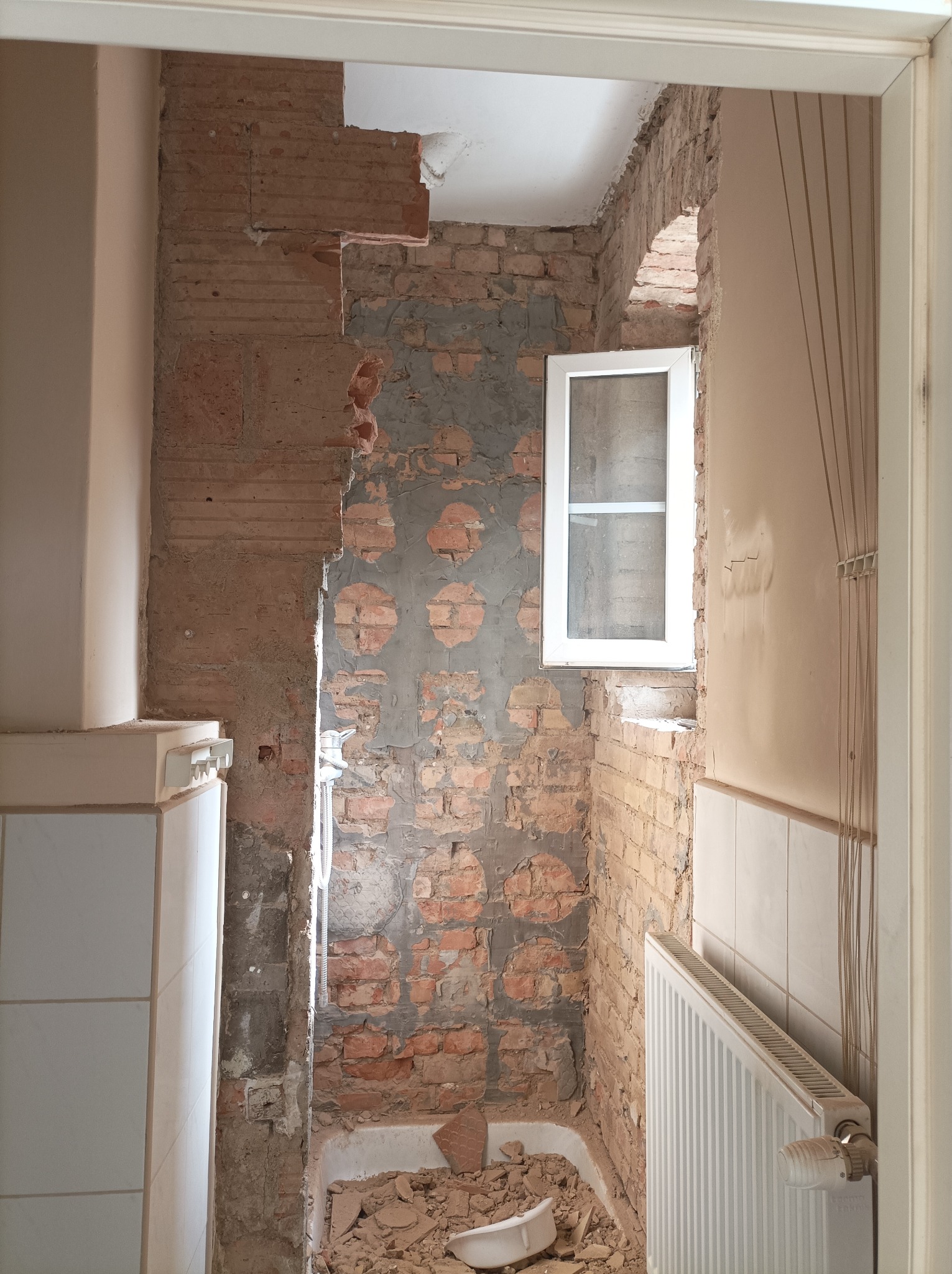 Łazienka w Zasutowie w trakcie demontażu starej glazury i przygotowania ścian z cegły pod nowe wykończenie, widoczne gruz i odsłonięte instalacje.