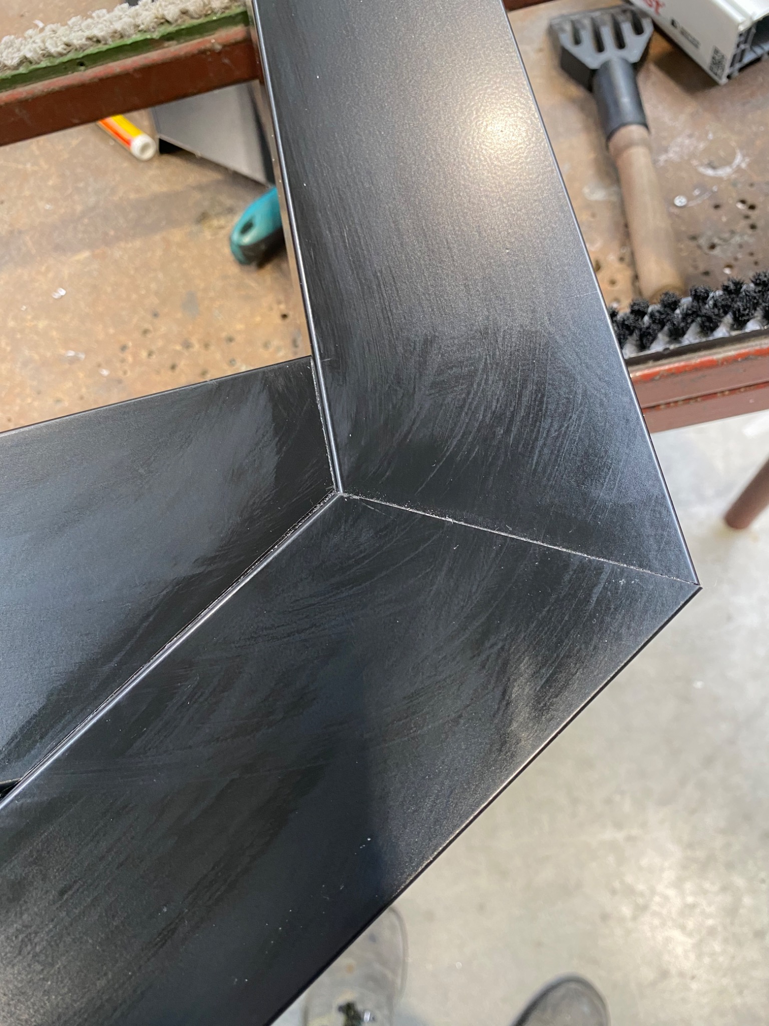 Szczegół narożnika czarnej ramy okiennej w warsztacie w Cikowicach, widoczne ślady obróbki i narzędzia na stole roboczym.