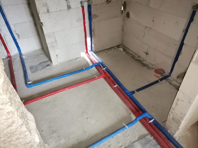 Instalacja wodna i grzewcza w surowym stanie, rury w izolacji czerwonej i niebieskiej prowadzone po ścianach z betonu komórkowego, zabezpieczone białymi opaskami zaciskowymi.