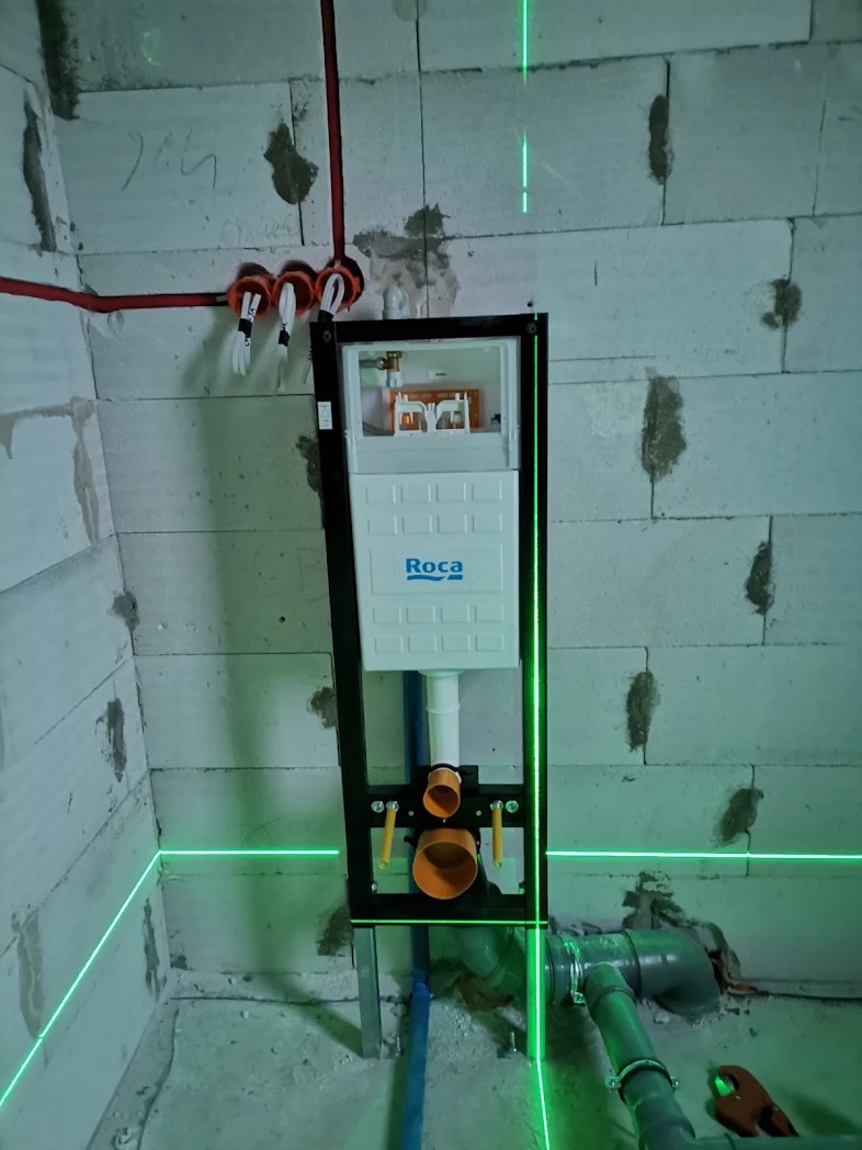 Montaż stelaża podtynkowego Roca w surowym wnętrzu z widocznymi instalacjami i poziomowaniem laserowym.