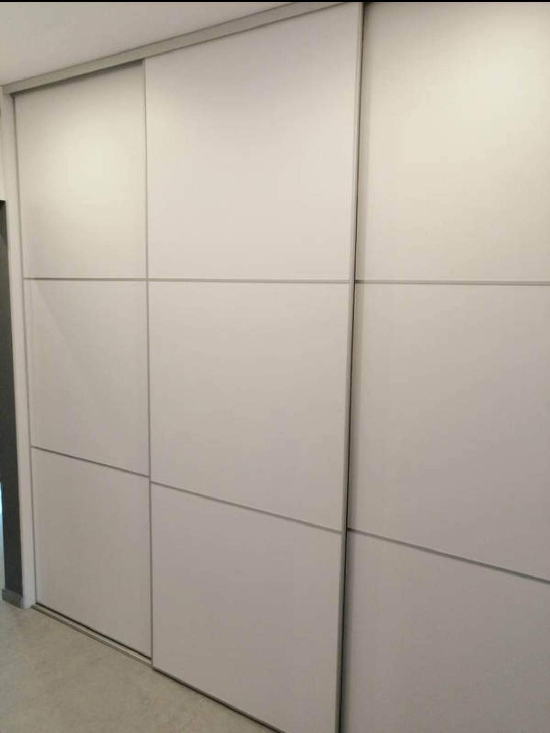 Biała szafa przesuwna z panelami, widoczna z bliskiej odległości, z delikatnym oświetleniem padającym na powierzchnię drzwi.