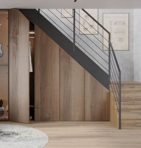 Drewniana zabudowa pod schodami z częściowo otwartą szafą, czarne metalowe barierki schodów, obrazy na ścianie, dywan na podłodze.
