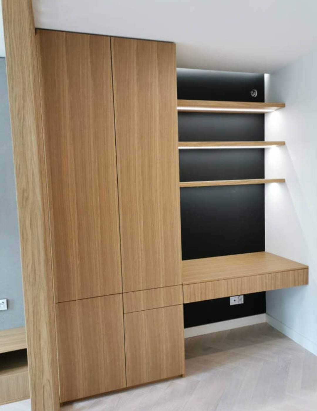 Drewniana zabudowa wnęki z szafą i biurkiem, oświetlenie LED pod półkami, jasna podłoga w jodełkę.