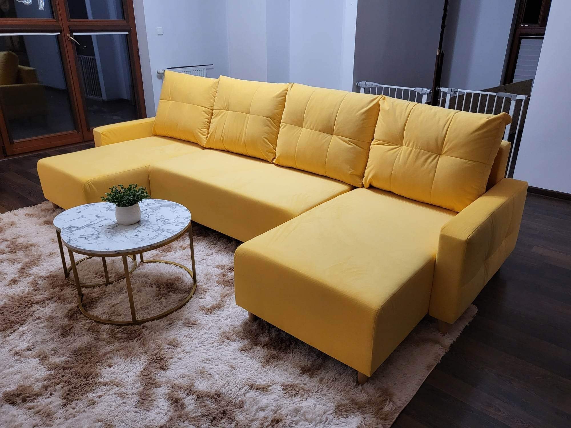 Żółta, modułowa sofa z poduszkami na tle puszystego dywanu i stolika kawowego z marmurowym blatem.