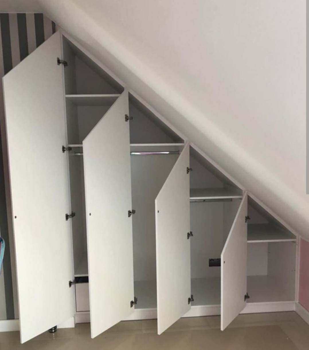 Biała szafa pod skosem dachu z otwartymi drzwiczkami ukazującymi półki i drążki na ubrania, widoczne zawiasy i minimalistyczne uchwyty.