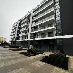 Clean Master 3City Professional cleaning firm - Nowoczesny, wielopiętrowy budynek apartamentowy z balkonami i przeszkloną fasadą, widoczny z poziomu chodnika wyłożonego kostką brukową. Szare niebo w tle.