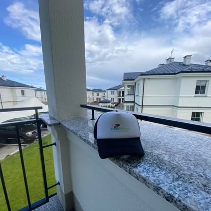 Czapka z logo firmy sprzątającej na marmurowym balkonie, w tle budynki mieszkalne i błękitne niebo. Prezentacja firmy sprzątającej.